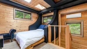 Een slaapkamer met een bed, een bureau en een stoel. Er zijn ramen en een airconditioning.