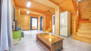 Een houten blokhut van binnen met een houten tafel, een witte koelkast en een groen kastje.