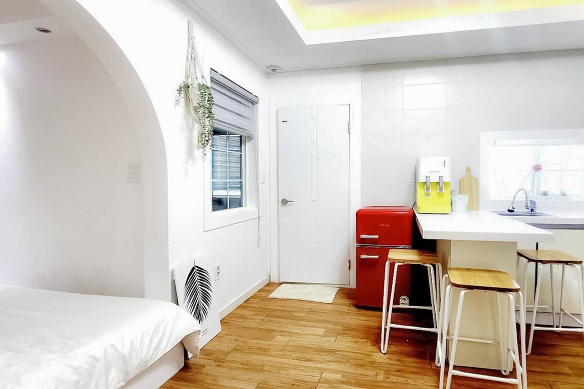 A compact bedroom with a bed, a small kitchenette, and a window with blinds.
