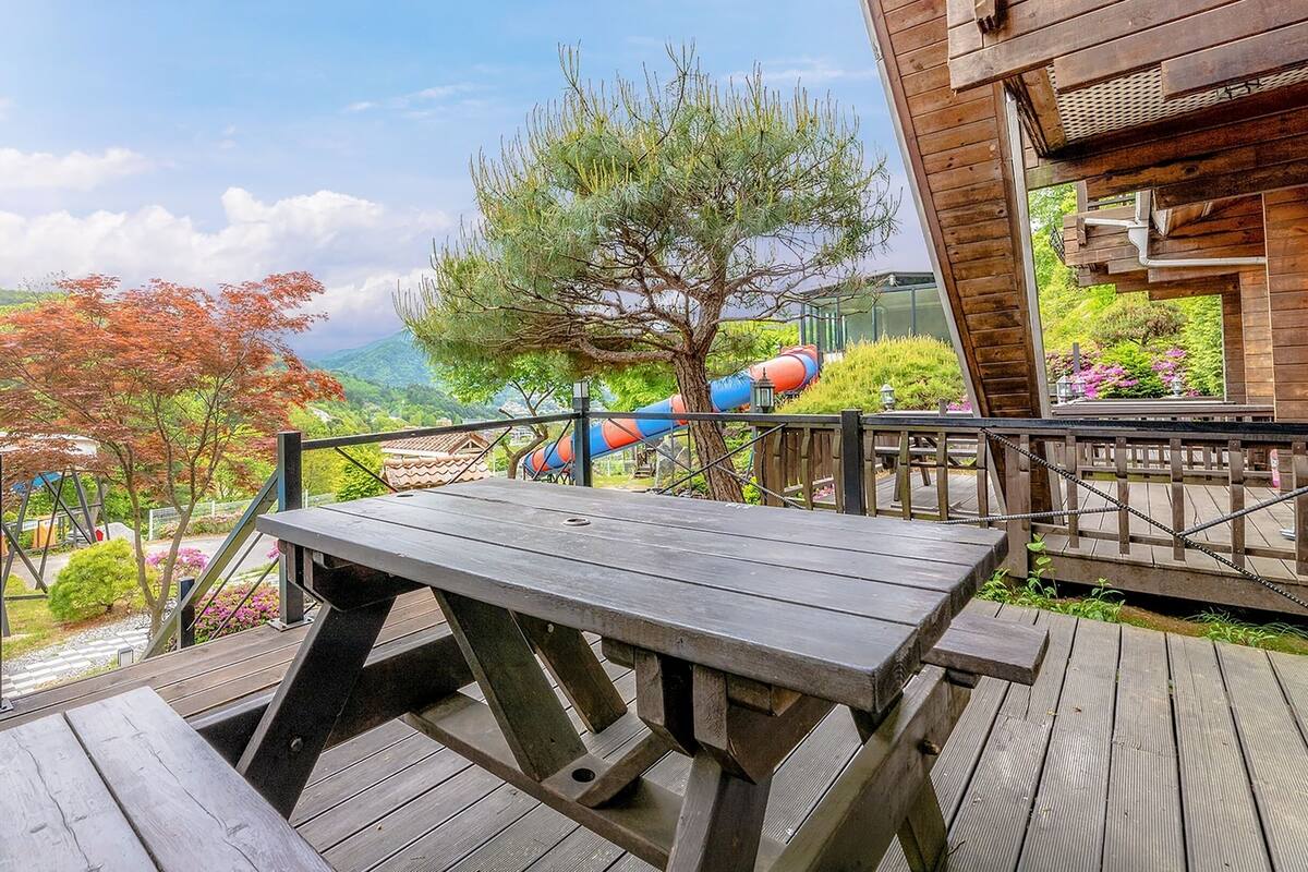 A wooden deck with a picnic table, overlooking a playground with slides and a mountain backdrop.