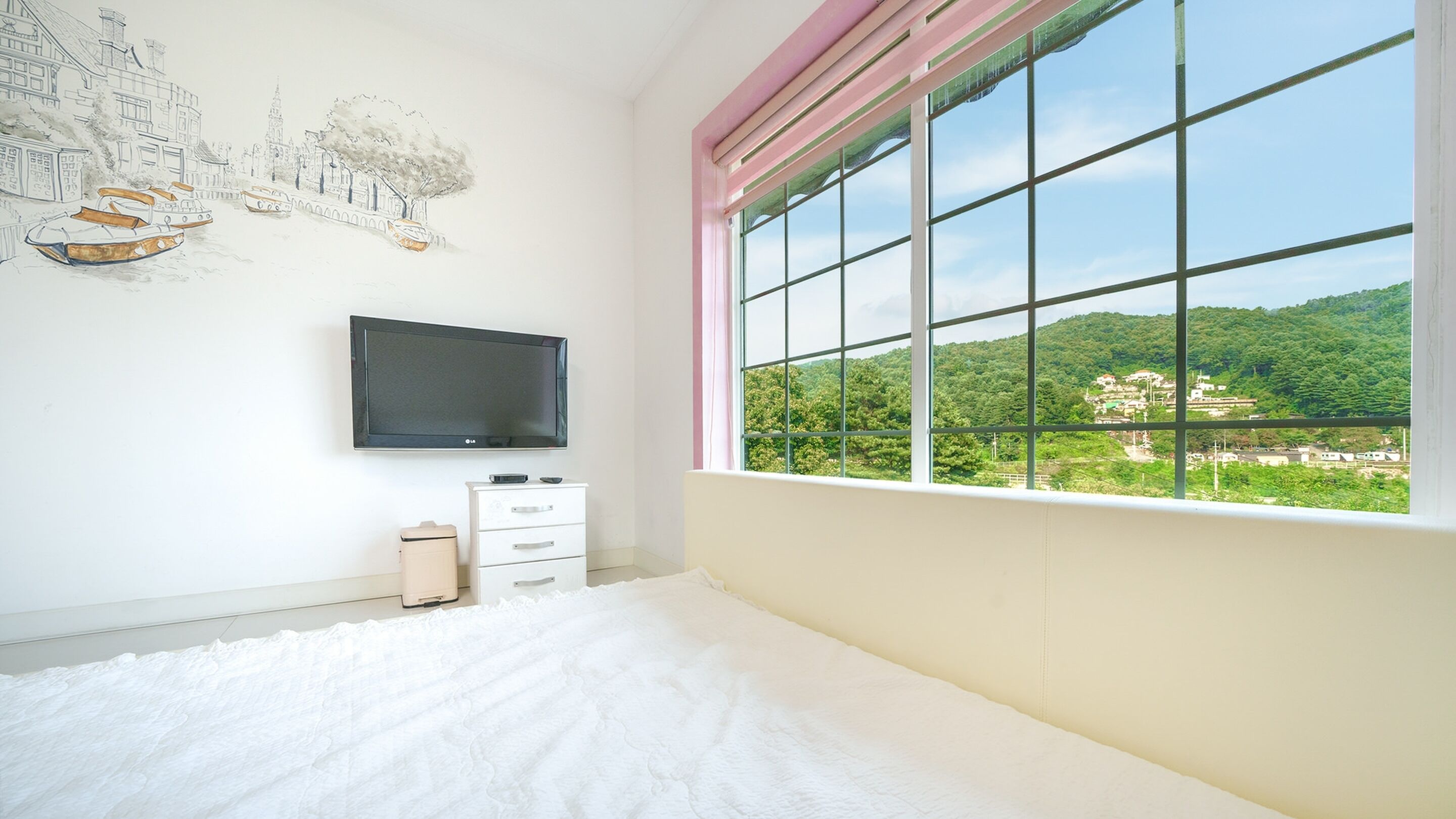 Ein Schlafzimmer mit großem Fenster, einem Flachbildfernseher, einem Bett und einer Kommode.