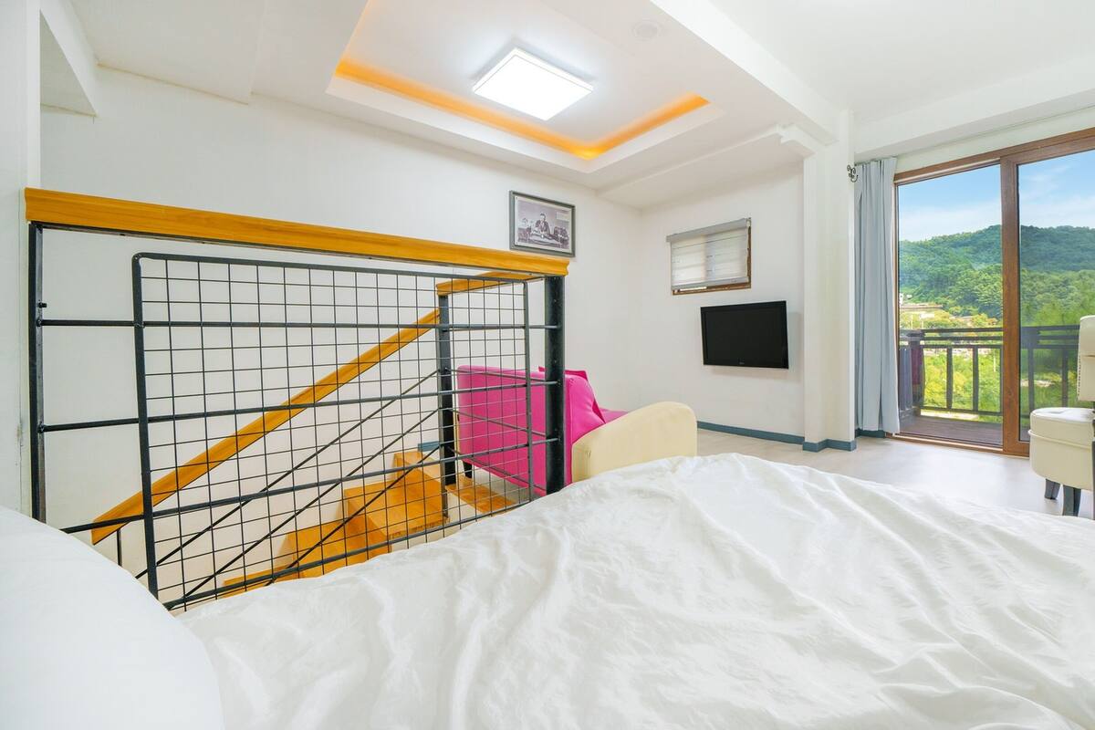 A hotel room with a bed, a TV, a balcony with a view, and a staircase.