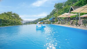 Une piscine avec un flotteur en forme de dauphin, un toboggan aquatique et des chaises longues.