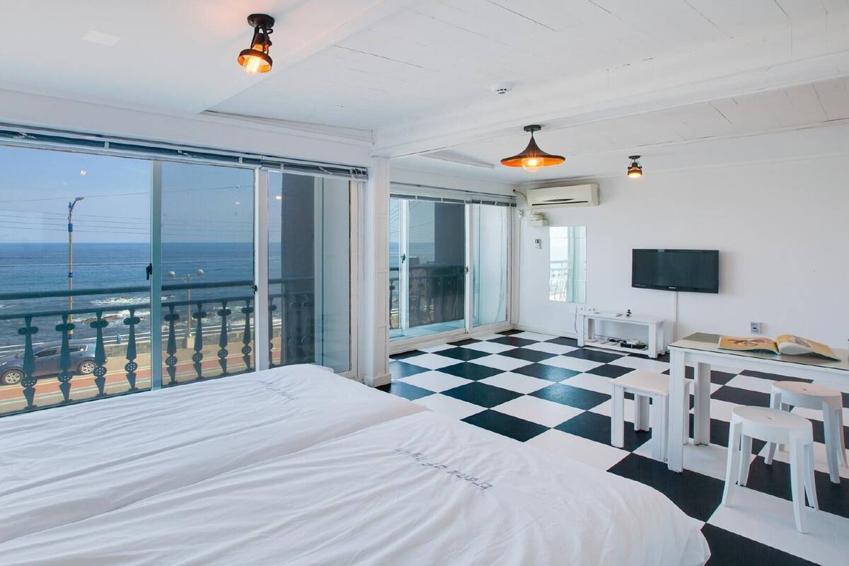 Ett hotellrum med en stor säng, ett skrivbord, en TV och en balkong med utsikt över havet.