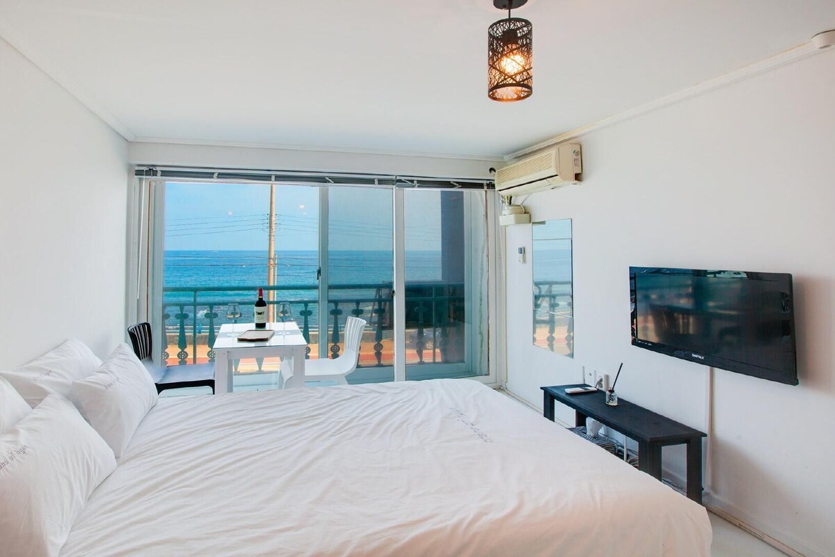 A bedroom with a large bed, a TV, and a balcony with a view of the sea.