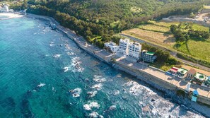 Vista aerea di una zona costiera con una strada che costeggia la spiaggia, edifici adiacenti alla strada e una visuale aperta sull'oceano.