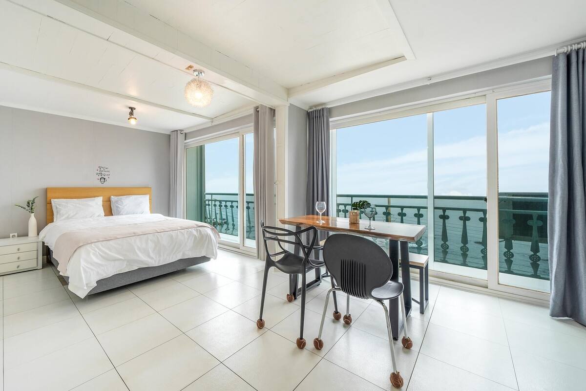 Ett modernt hotellrum med en stor säng, ett matbord med stolar och en balkong med utsikt över havet.