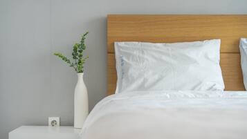 A neatly made bed with white bedding, a wooden headboard, and a white vase with green foliage on a bedside table.