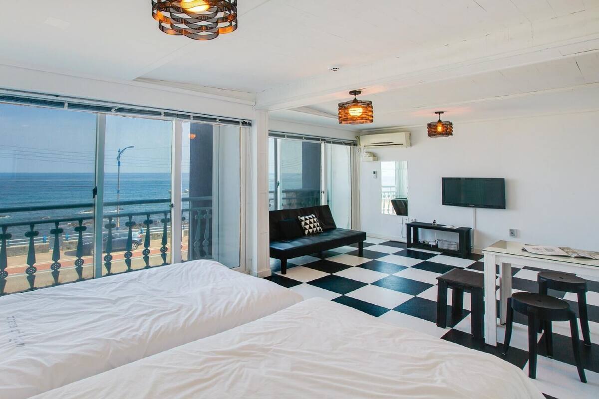 Ett hotellrum med en stor säng, ett skrivbord, en TV och en balkong med utsikt över havet.