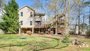 A two-story house with a deck, a covered patio, and a yard with a lawn and trees. - Pet-Friendly Lakehouse: View Tower + Fire Pit! (Leesville)