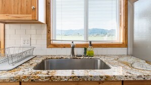 A kitchen with a granite countertop, stainless steel sink, wooden cabinets, and a window with blinds. - Dog Friendly Puget Island Home on the Columbia River. Secure Private Moorage!! (Cathlamet)