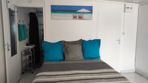 Ein Schlafzimmer mit Bett, einem Strandbild und einem Badezimmer mit Waschbecken und Handtuchhalter.