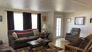 A living room with a sofa, armchair, and a coffee table. There is a door with a window, a lamp, and a rug on the floor.