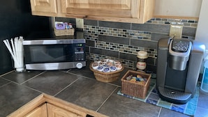 A kitchen with a microwave, coffee maker, and baskets of snacks.
