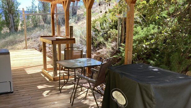 A wooden deck with a table and chairs, a grill, and a covered area.