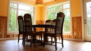 A dining area with a wooden table and chairs, large windows, and a hanging light fixture.