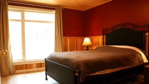 A bedroom with a bed, a window with curtains, and a nightstand with a lamp.