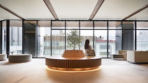 Un vestíbulo moderno con un mostrador de recepción de madera en el centro, ventanas amplias y asientos contemporáneos.