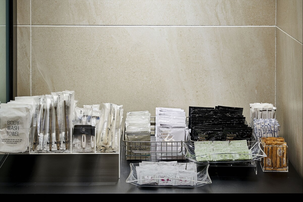 Un baño de hotel con varios artículos de aseo y comodidades organizados cuidadosamente en estantes y encimeras.