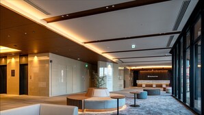 Un moderno vestíbulo de hotel con zonas de estar, un mostrador de recepción y amplias ventanas.
