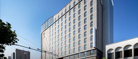 A modern hotel building with a prominent logo, multiple floors, and a glass facade.