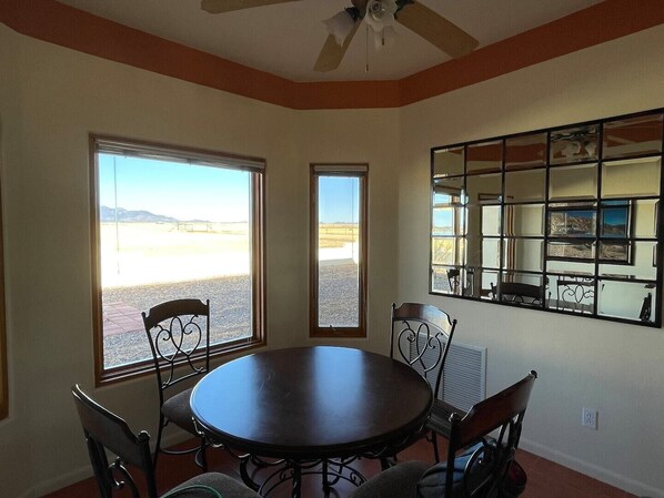 A dining area with a round table and chairs, large windows with a view of a desert landscape, and a ceiling fan.