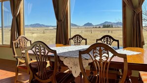 A dining area with a table and chairs, large windows with curtains, and a view of a field and mountains. - Peaceful SW-style ranch home in wine country (Elgin)