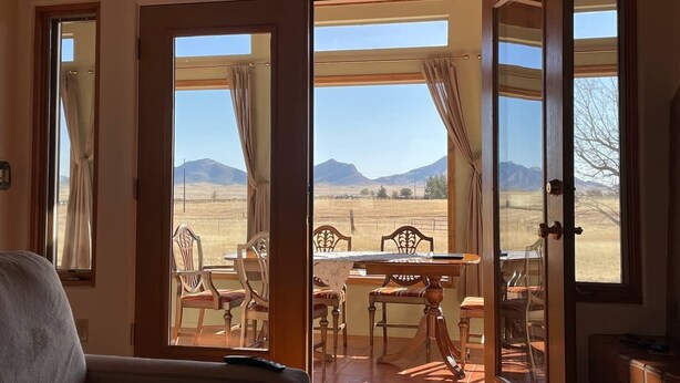 A room with a large sliding glass door leading to an outdoor patio with a table and chairs, a view of mountains, and a wooden ceiling. - Peaceful SW-style ranch home in wine country (Elgin)