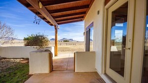 A covered patio with a concrete floor, two white planters, and a door leading to a view of mountains. - Peaceful SW-style ranch home in wine country (Elgin)