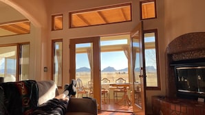 A spacious living room with a large window, a fireplace, and a dining area with outdoor seating. - Peaceful SW-style ranch home in wine country (Elgin)