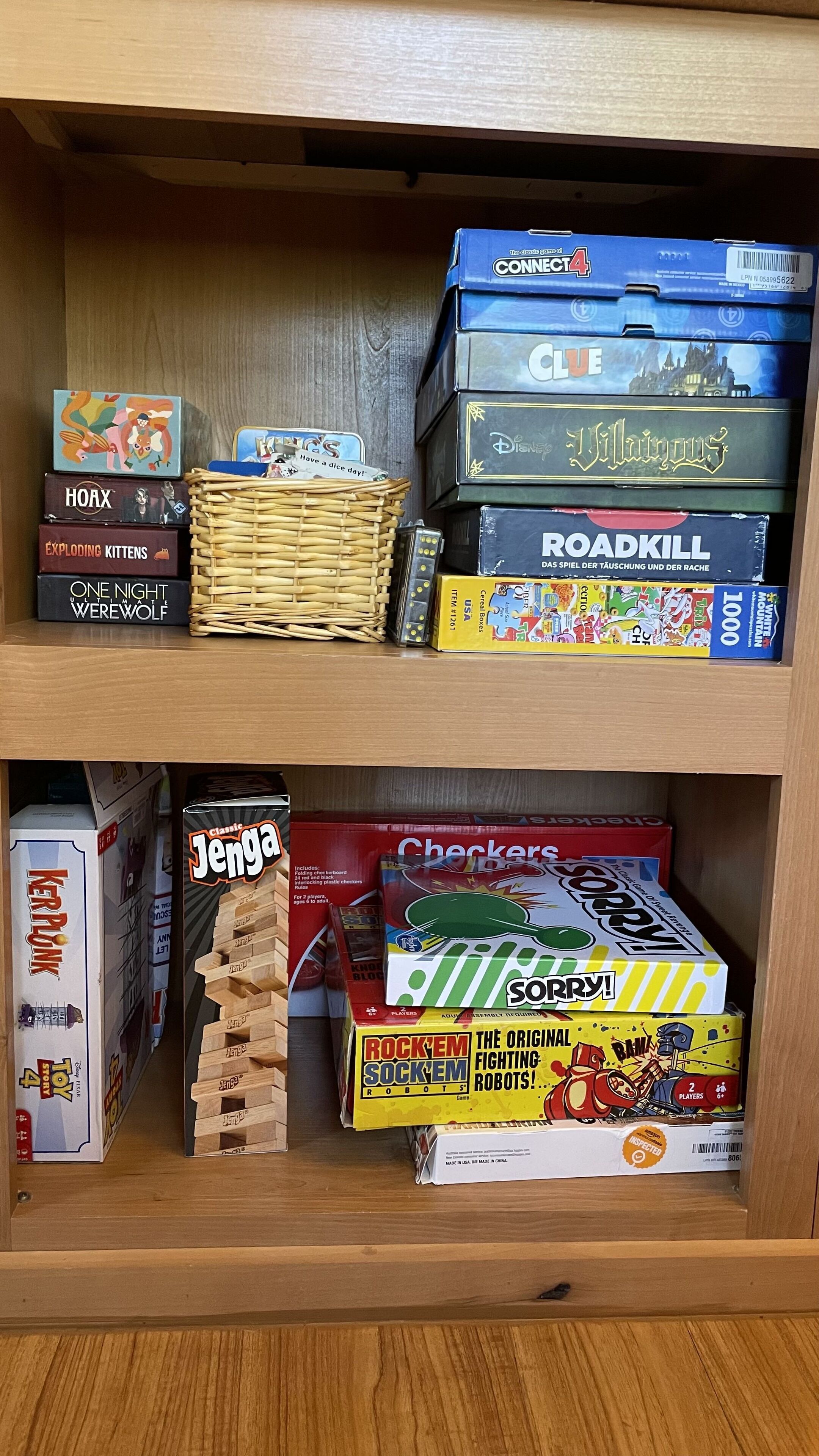 Ein Holzregal mit verschiedenen Gesellschaftsspielen, darunter Connect 4, Disney's Walt Disney World und Jenga.
