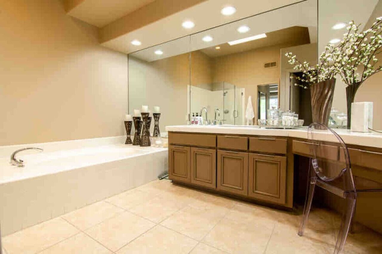 Un baño moderno con una bañera grande, un tocador con espejo y un florero con flores.