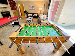 Una mesa de fútbol de mesa en una habitación con un sofá, una lámpara y una ventana.