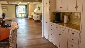 Un vaste espace de vie doté d’un plancher en bois, d’une table à manger avec des chaises et d’un coin cuisine équipé de placards et d’une machine à café.