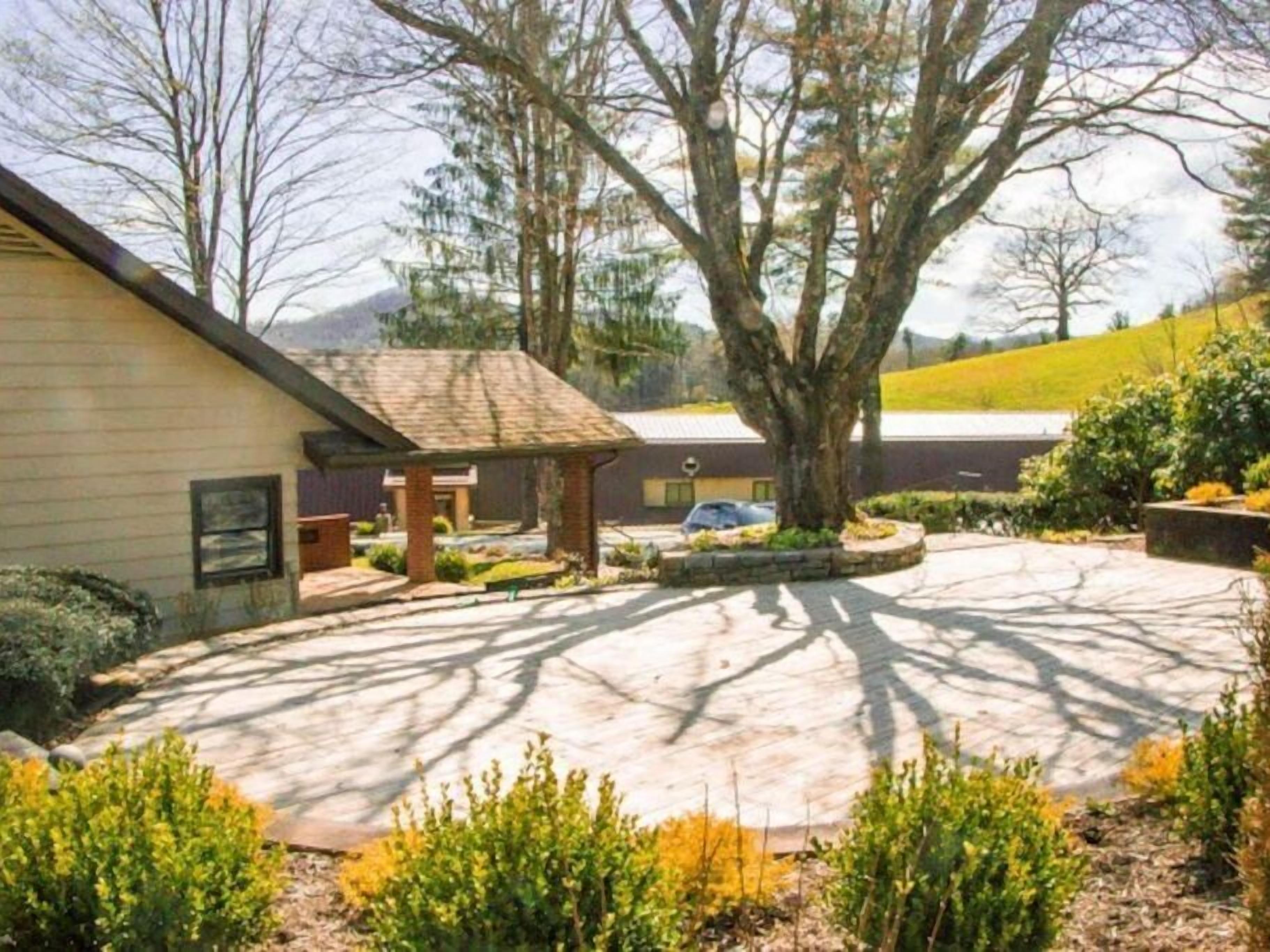 A residential property with a covered patio, a driveway, and a large tree providing shade.