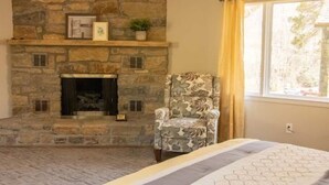 Une pièce dotée d’une cheminée en pierre, d’un fauteuil à motifs et d’un lit recouvert d’une couvre-lit à motifs géométriques.