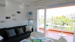 A room with a black sofa, a dining table with chairs, a balcony with a white railing, and a view of buildings and greenery. - InmoBooking Mercurio, heated and close to the beach (Salou)