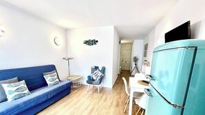 En kompakt opholdsstue med en blå sofa, et lille rundt bord, en blå stol, et hvidt spisebord og et turkis køleskab.