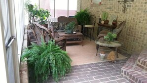 Uma área de pátio acolhedora com móveis de vime, plantas em vasos e piso de tijolos.
