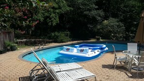 Uma piscina com um flutuador inflável azul, cadeiras de praia brancas e uma mesa com cadeiras.
