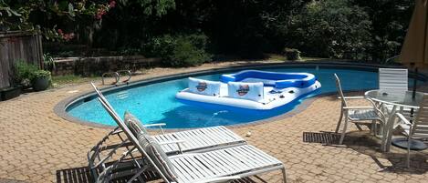 Una piscina con un flotador inflable azul, sillas de descanso blancas y una mesa con sillas.