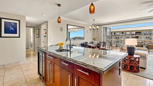 A modern kitchen with a large island, a dining area with a view, and a living room with a fireplace. - Maui Resort Rentals: Honua Kai Konea 649, Gorgeous 6th Floor 3BR w/ Stunning Ocean and Black Rock Views! (Lahaina)