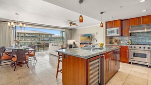 A modern kitchen with a large island, stainless steel appliances, and a dining area with a view. - Maui Resort Rentals: Honua Kai Konea 649, Gorgeous 6th Floor 3BR w/ Stunning Ocean and Black Rock Views! (Lahaina)