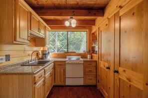 A wooden cabin-style kitchen with a stove, sink, and cabinets.
