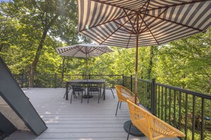 A deck with a table and chairs, surrounded by a railing, and shaded by striped umbrellas.