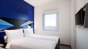 Une chambre d’hôtel moderne avec un grand lit, un téléviseur fixé au mur et une fenêtre donnant sur la ville.