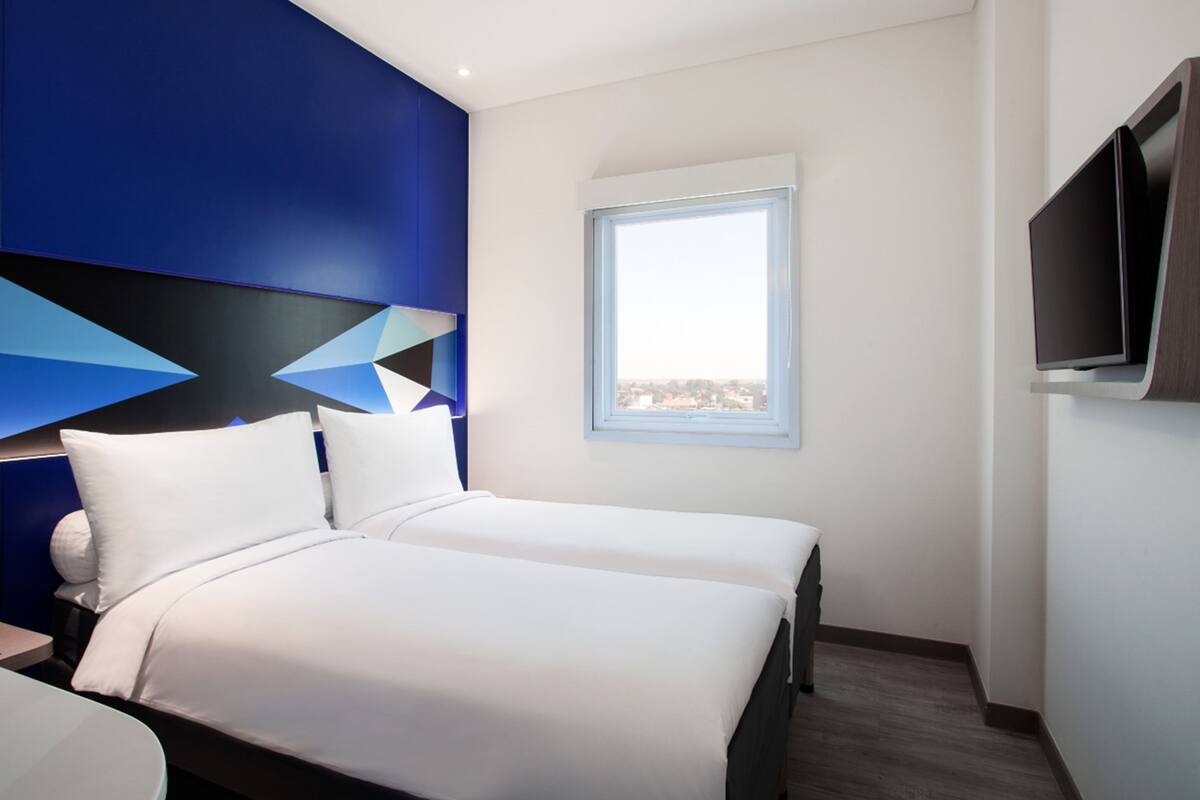Une chambre d’hôtel moderne avec un grand lit, un téléviseur fixé au mur et une fenêtre donnant sur la ville.
