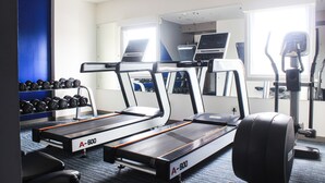 Une salle de sport équipée de tapis de course, d’un rameur et d’haltères.