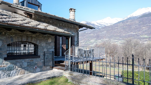 A stone building with a balcony, a metal fence, and a mountainous backdrop. - Maison Pro de Solari by Interhome (Fenis)