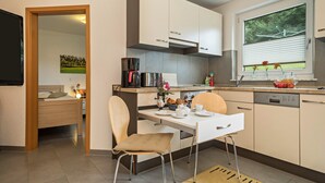 Une cuisine moderne avec un coin repas, une machine à café et une fenêtre donnant sur un espace verdoyant.